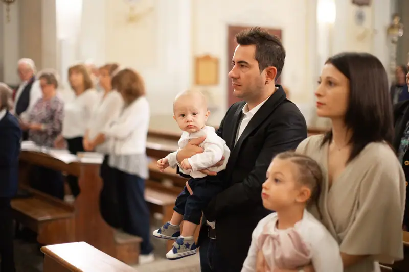 In chiesa, durante il battesimo di Elia: un uomo con il bambino in braccio, accanto una donna e una bambina