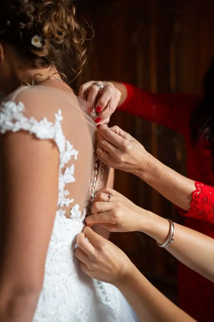 Due mani allacciano i bottoni di pizzo sulla schiena della sposa