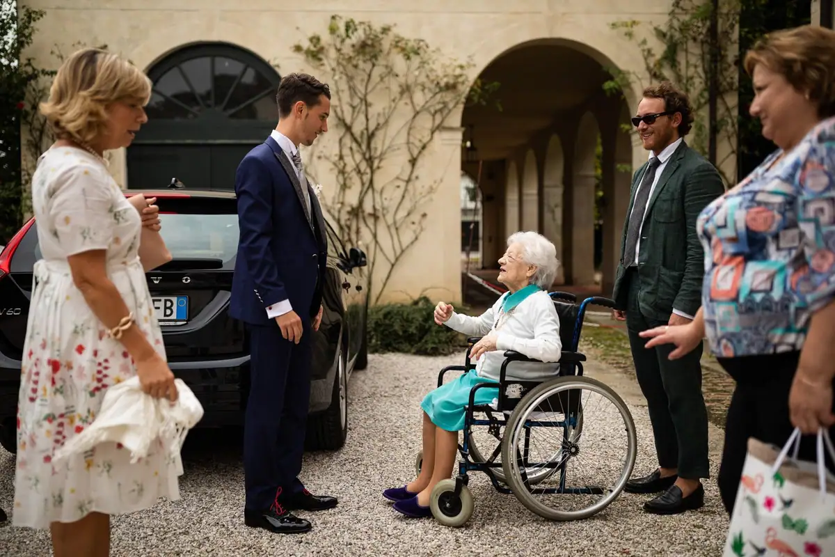 I primi invitati nel cortile della villa, fra loro una signora in carrozzina che sorride