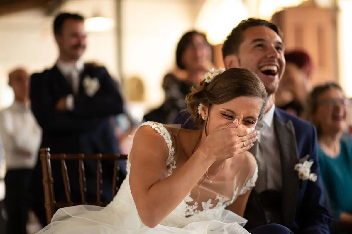 La sposa ride coprendosi la bocca con la mano, lo sposo accanto a lei che ride a sua volta
