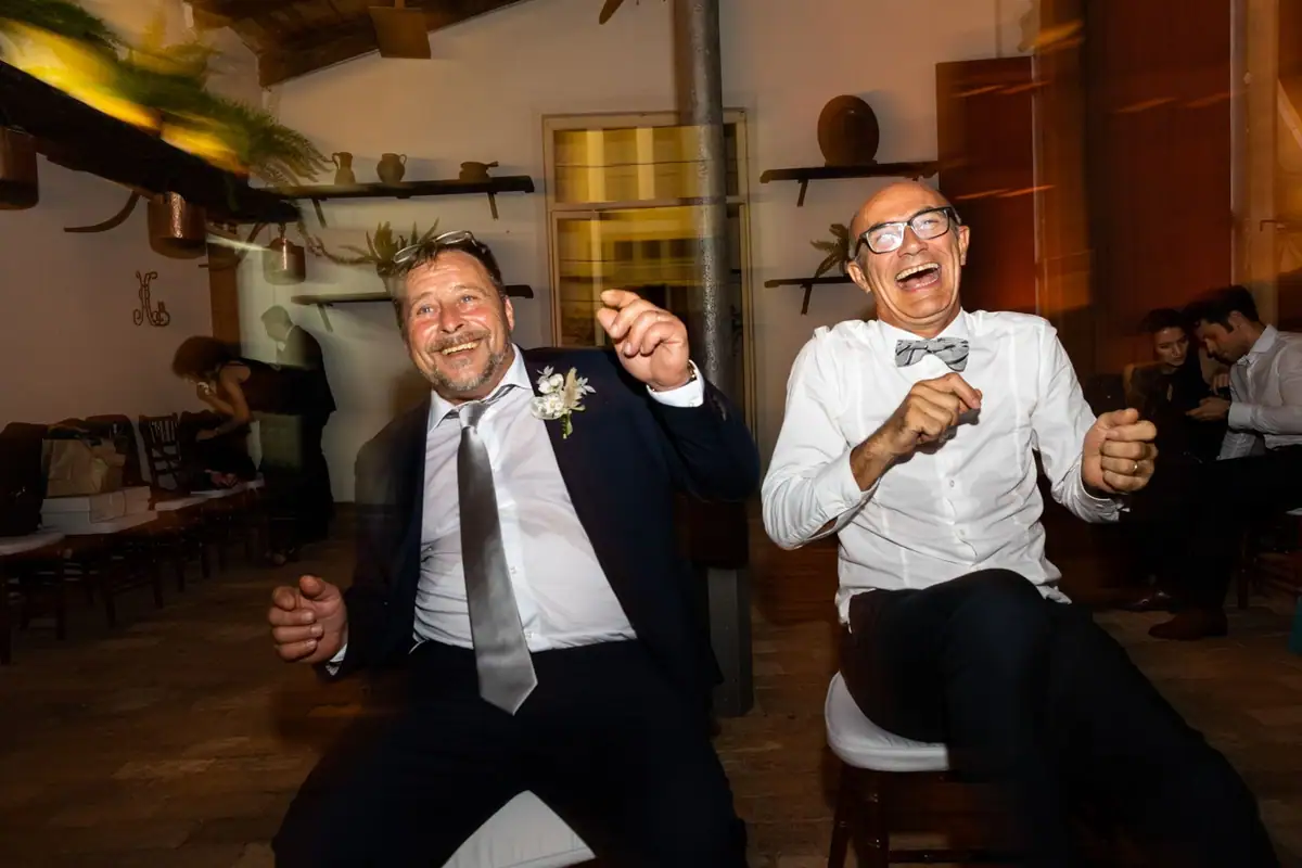 Due invitati ballano scatenati e ridono, uno con la camicia aperta e il papillon slacciato